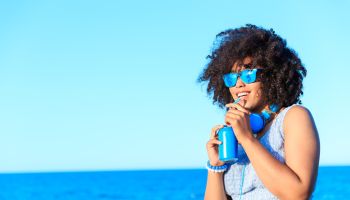 African woman in blue outfit drinking cocktail on beach